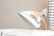 Woman Is Ironing Clothes. The Girl Holds An Iron On An Ironing Board.