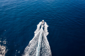 Wall Mural - aerial view of a speedboat traveling over blue sea leaving a trail of white waves and bubbles behind