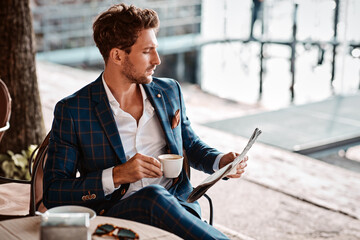 handsome man drinking coffee and reading newspaper in cafe