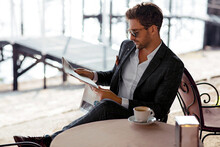 Handsome Man Drinking Coffee And Reading Newspaper In Cafe