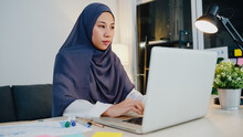 Beautiful Asia Muslim Lady In Headscarf Casual Wear Using Laptop In Living Room At Night House. Remotely Work From Home, New Normal Lifestyle, Social Distance, Quarantine For Corona Virus Prevention.