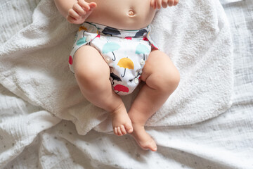 A baby lying on a bed with the focus on the baby's legs and cloth diaper with a pretty umbrella print