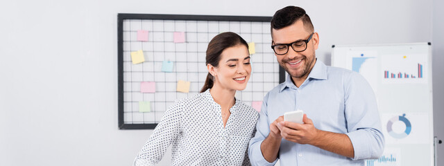 happy business people looking at smartphone in office, banner