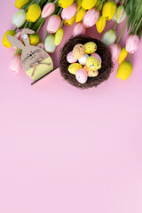 Easter composition with colorful quail eggs in nest, wooden bunny and tulips on pink background. Flat lay. Spring composition. Happy easter greeting card. Copy space.