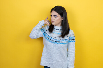 Wall Mural - Young caucasian woman wearing casual sweater over yellow background confused doing phone gesture with hand and fingers like talking on the telephone