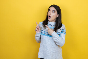 Wall Mural - Young caucasian woman wearing casual sweater over yellow background surprised and pointing her fingers side