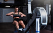 Young strong fit sweaty powerful attractive muscular woman with big muscles doing hard core row heavy training workout on indoor rower at the gym real people rowing exercise