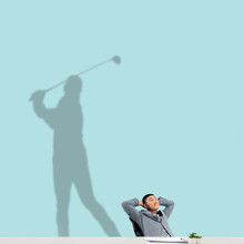 Young Asian Man Dreaming About Future In Big Sport During His Work In Office. Becoming A Legend. Shadow, Silhouette Of Professional Golf Player On The Wall. Inspiration, Aspiration. Copyspace.