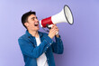 © luismolinero - Teenager caucasian  handsome man isolated on purple background shouting through a megaphone