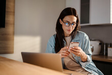Serious Charming Woman Using Smartphone While Working With Laptop