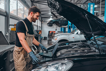 Mechanic with laptop near car engine. Modern car diagnostic program.