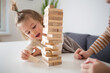 children play board game jenga. girls build tower of wooden blocks, concept of developing fine motor skills, home joint games. Leisure activities for children at home