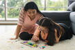 © amornchaijj - young girl with autism is practicing playing with toys on the floor at home with his mother. Autistic young students are learning with teachers.