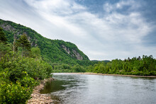 "Peaceful River Meandering
 Down At Summer Time During A Cloudy Day With Green Trees And Cliffs On Its Edge Between Tadoussac And Saguenay Near The Fjords Du Saguenay"