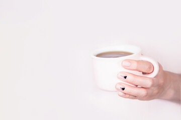 Wall Mural - Hand holding pink cup of black tea on pale pink background, copy space