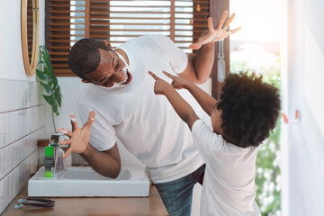 African American Man and little boy having fun laughing with shaving foam on face in bathroom at home.