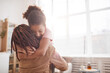 © Seventyfour - Minimal waist up portrait of happy African-American girl embracing mother in cozy home interior lit by sunlight, copy space