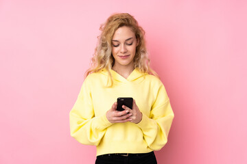 Poster - Young blonde woman wearing a sweatshirt isolated on pink background sending a message with the mobile