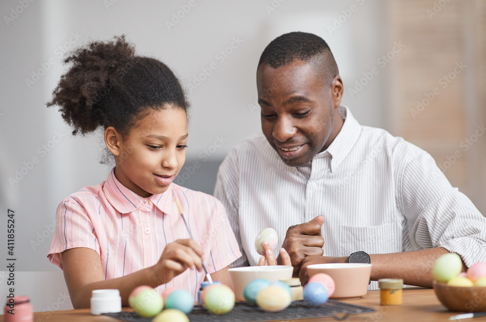 Minimal portrait of young African-American girl painting Easter eggs while enjoying DIY decorating with father - obrazy, fototapety, plakaty 
