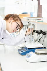 Wall Mural - In a chemical laboratory, a girl laboratory assistant drips a solution into a measuring beaker with a special pipette