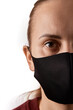© 5M - Vertical close up portrait of a young european woman with brown eyes wearing black face mask, covering her nose, looking straight at camera, isolated over white background, copy space on the left.