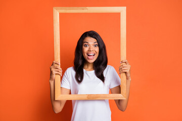 Poster - Portrait of impressed girl wear white t-shirt hold frame isolated on orange color background