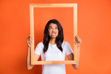 Photo of crazy lady hold wooden frame squint bite lip wear white t-shirt isolated orange color background