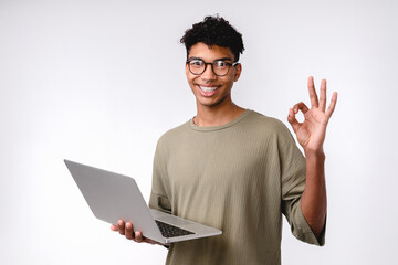 Happy young mixed-race student showing okay sign using laptop isolated over white background