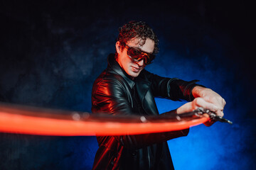 Dangerous and martial guy dressed in black leather clothing with sunglasses poses in blue background holding sword.