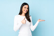 Young caucasian woman isolated on blue background holding copyspace imaginary on the palm to insert an ad and with thumbs up