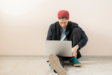 a young male person working at home with laptop, online freelancer lifestyle sitting near the wall isolated