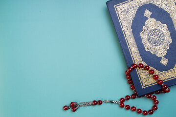 Ramadan Kareem, Eid Mubarak or Islamic concept. The Islamic holy book, Quran or Kuran, with rosary beads or “tasbih” on grey background. Arabic words on the book means 