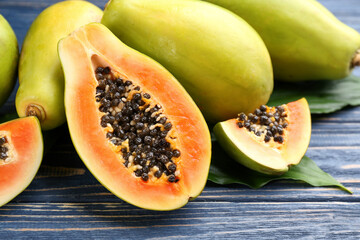 Fresh ripe papaya fruits with green leaves on wooden table, closeup