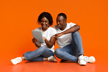 Smiling african american lovers using digital tablet over orange