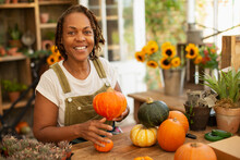 Portrait Happy Female Florist Arranging Autumn Pumpkins In Shop