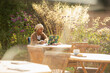 © Martin Barraud/Caia Image - Woman working at laptop on sunny garden cafe patio