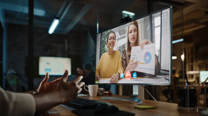 Wall Mural - Handsome Black African American Project Manager is Making a Video Call on Desktop Computer in a Creative Office Environment. Male Specialist Talking to a Two Female Colleagues Over a Live Camera.