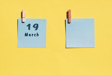 March 19st. Day of 19 month, calendar date. Two blue sheets for writing on a yellow background. Top view, copy space. Spring month, day of the year concept