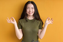 Female Enjoys Meditation, Isolated In Studio On Yellow Background. Young Woman With Long Black Hair Stands Smiling In Yoga Pose, Keep Calm. Yoga Concept