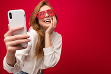 Attractive Charming Young Smiling Happy Woman Holding And Using Mobile Phone Taking Selfie Wearing Stylish Clothes Isolated Over Wall Background