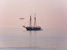 Silhouette Of A Beautiful Sailing Ship At Anchor With Lowered Sails And A Soaring Seagull Over The Absolutely Calm Waters Of The Ligurian Sea,