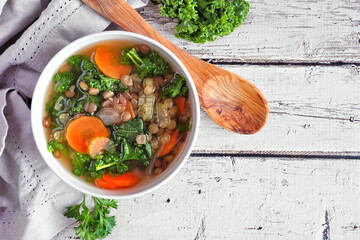 Sticker - Healthy vegetable soup with kale and lentils. Overhead view table scene on a rustic white wood background.