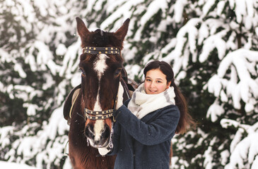 Cute teenage girl with a horse in winter in the woods. Communicating with animals