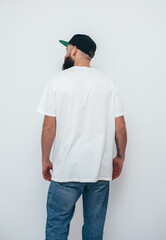 Wall Mural - Young bearded hipster guy wearing white oversized blank t-shirt on a white background. Mock-up for print. T-shirt design and advertising concept.