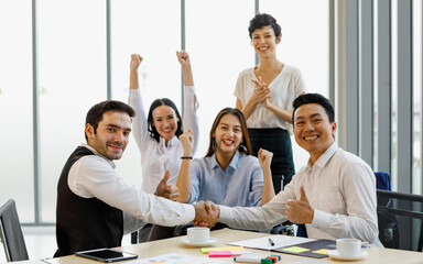 Two diversity male businesspeople make a hand shake together with trust and joyful while other team pose in congratulation and greet manners.