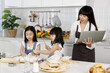 © Bangkok Click Studio - Family group photo of 30s mom and two little girls, 3 years and 7 years old, learning how to make bread and bakery. Mother opening a notebook computer to find food formula in modern kitchen