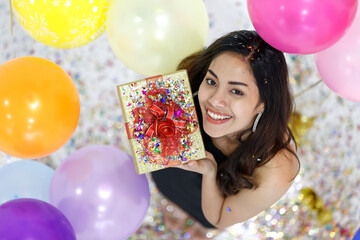 Two young and beautiful sexy Asian girls with colorful gift box dancing and playing with fun and happiness in a party with the bright color balloon in the background. Taken from a top-down angle.