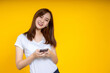 © jumlongch - Smiling young Asian woman is pointing on smartphone standing on yellow background.