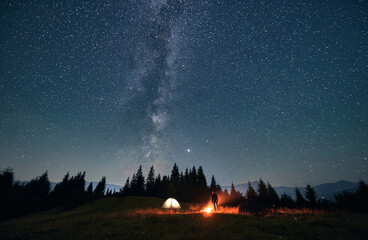 silhouette of male traveler near illuminated camp tent under beautiful night sky with stars. magnifi