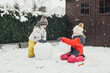 © Elena Medoks - Snow time, games in the snow. Cute Caucasian children brother and sister make a snowman in the yard of their house. Fun during quarantine